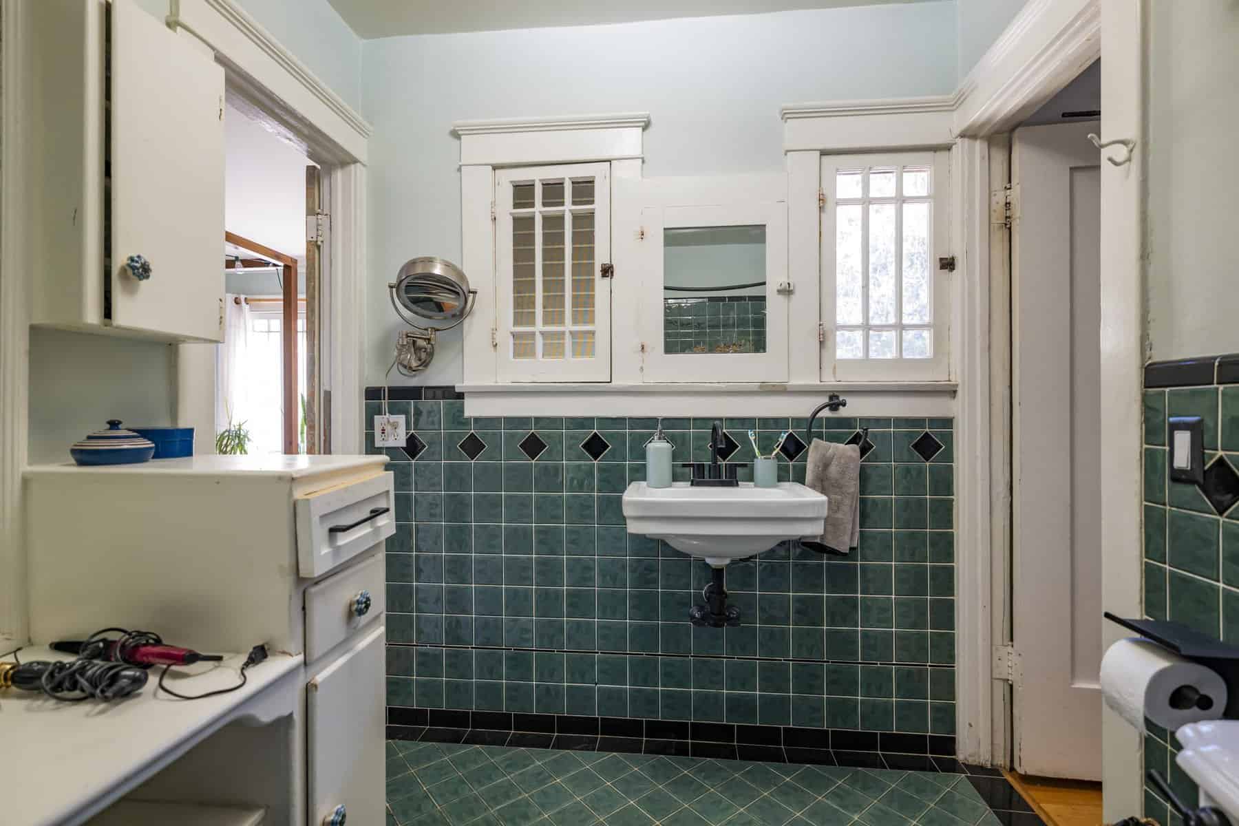 Vintage-style bathroom with green square tiles, white wall cabinets, and a wall-mounted sink