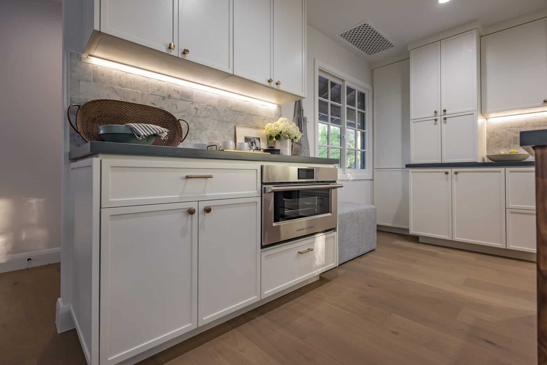 Kitchen with white cabinetry, a built-in microwave, marble backsplash, and under-cabinet lighting