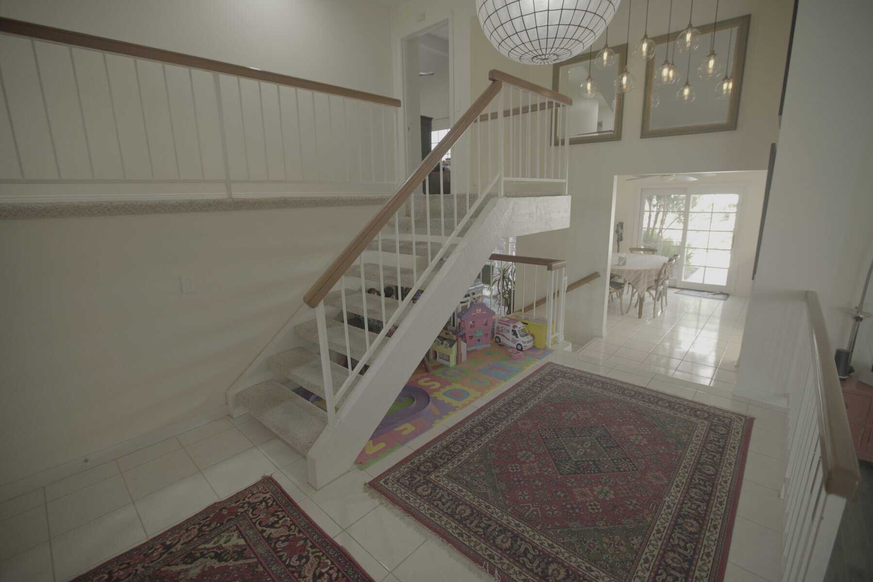 A two-story foyer with a white staircase, a patterned rug, and a chandelier
