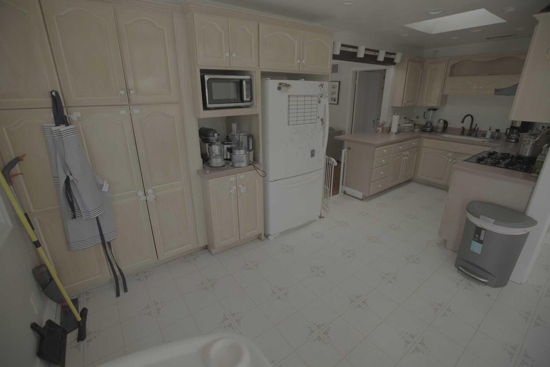 Organized kitchen with wooden cabinets, a white refrigerator, and cleaning tools stored on the side