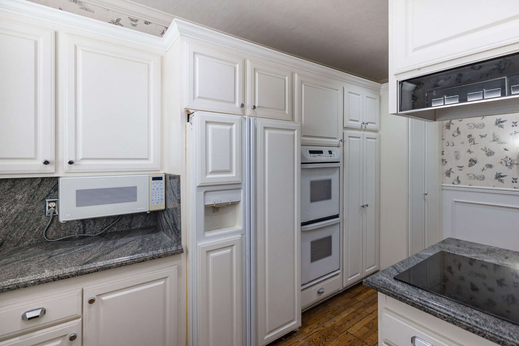White kitchen with double ovens, granite counters, and built-in microwave