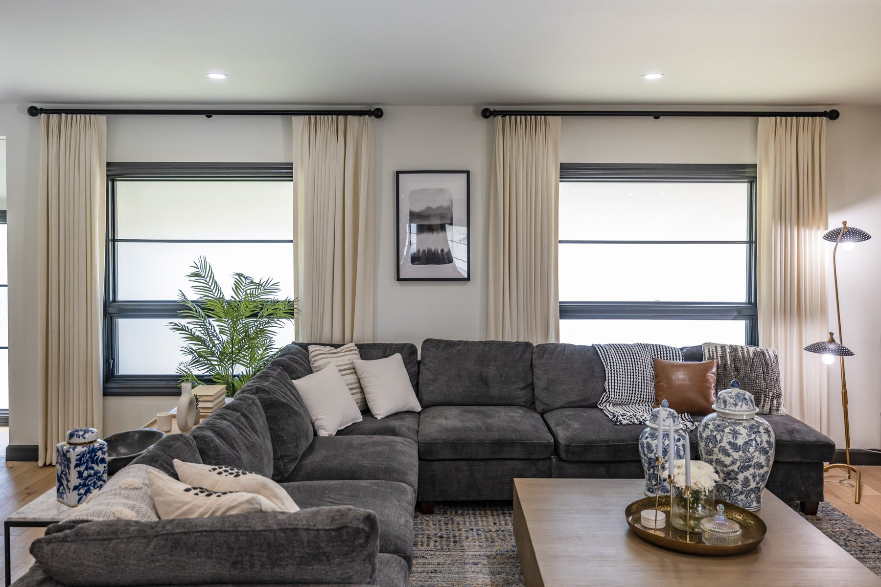 Living room with dark gray sectional cream curtains black window trim and decorative accents