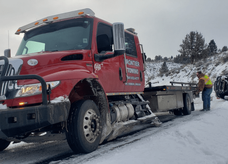 Red towing truck from Frontier Repair & Towing on snowy road with worker nearby.