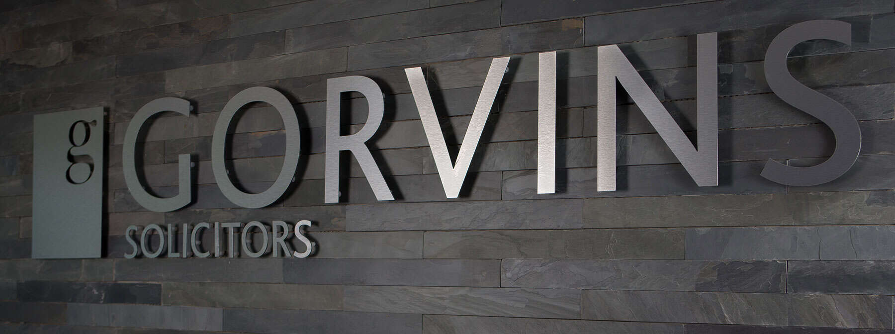 Modern law firm reception area with the 'Gorvins Solicitors' logo on a textured grey brick wall.