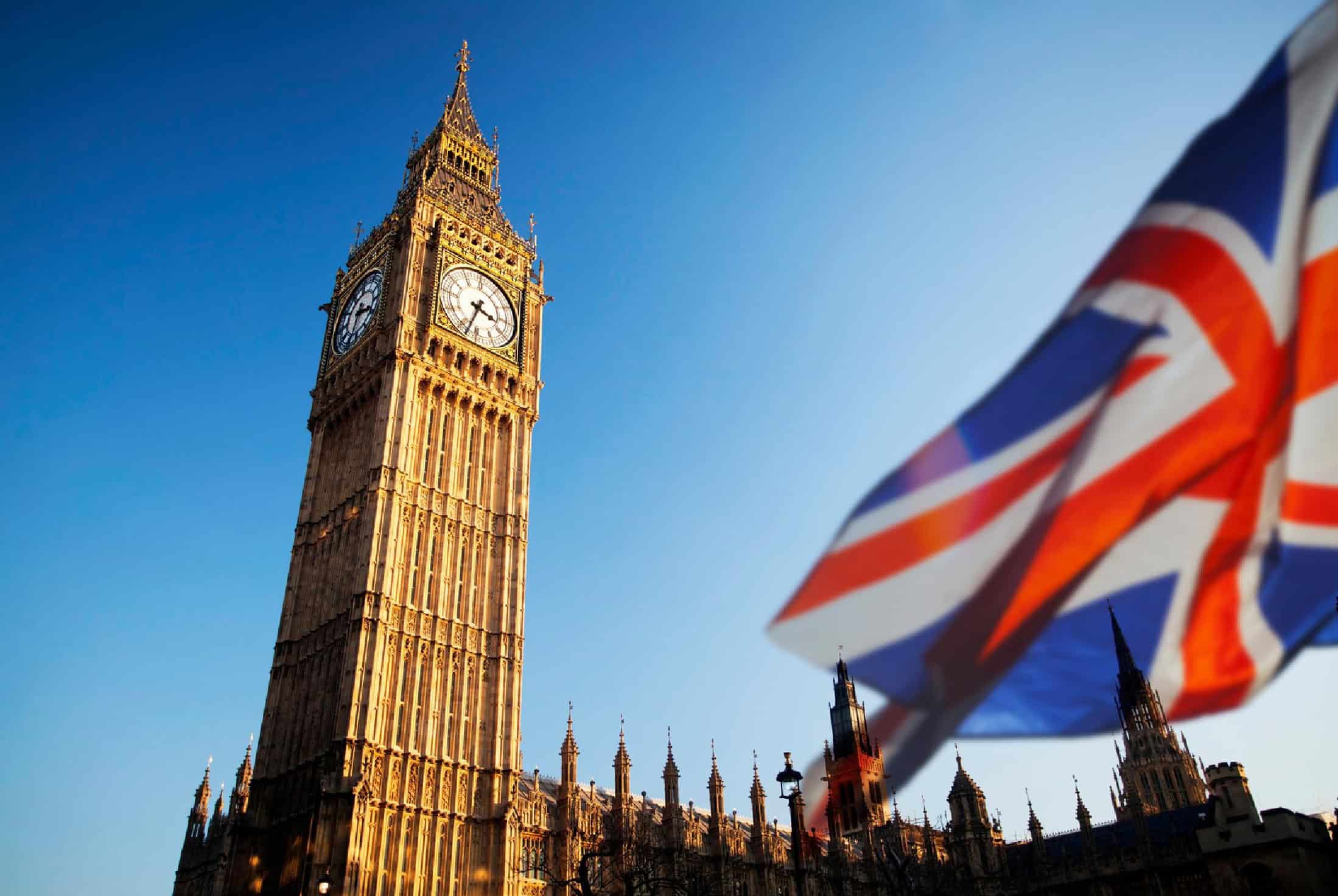 London Big Ben and Union Jack flag flying in the foreground, showcasing iconic British landmarks and patriotic symbols against a clear blue sky.