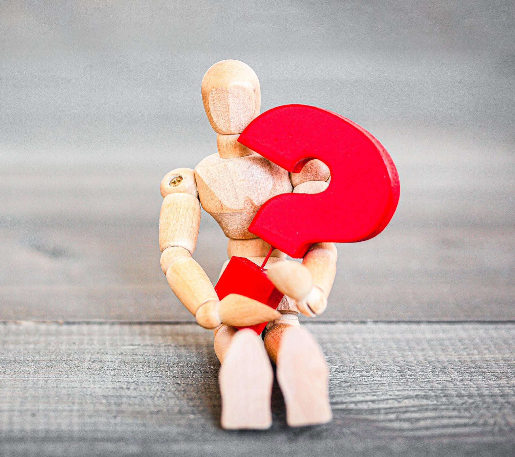Wooden artist mannequin holding a red question mark symbol.
