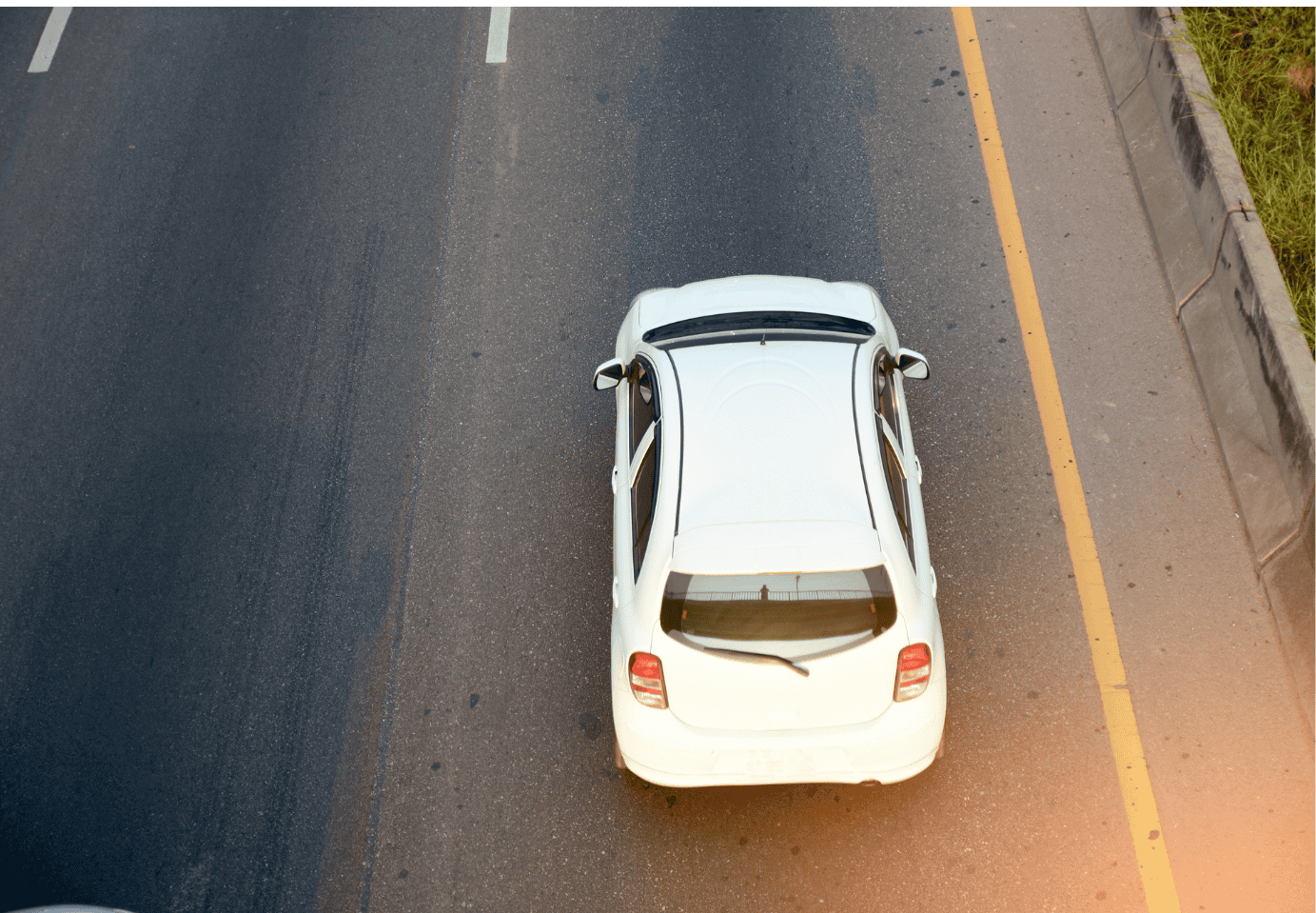 White hatchback car parked on asphalt road from an aerial view.