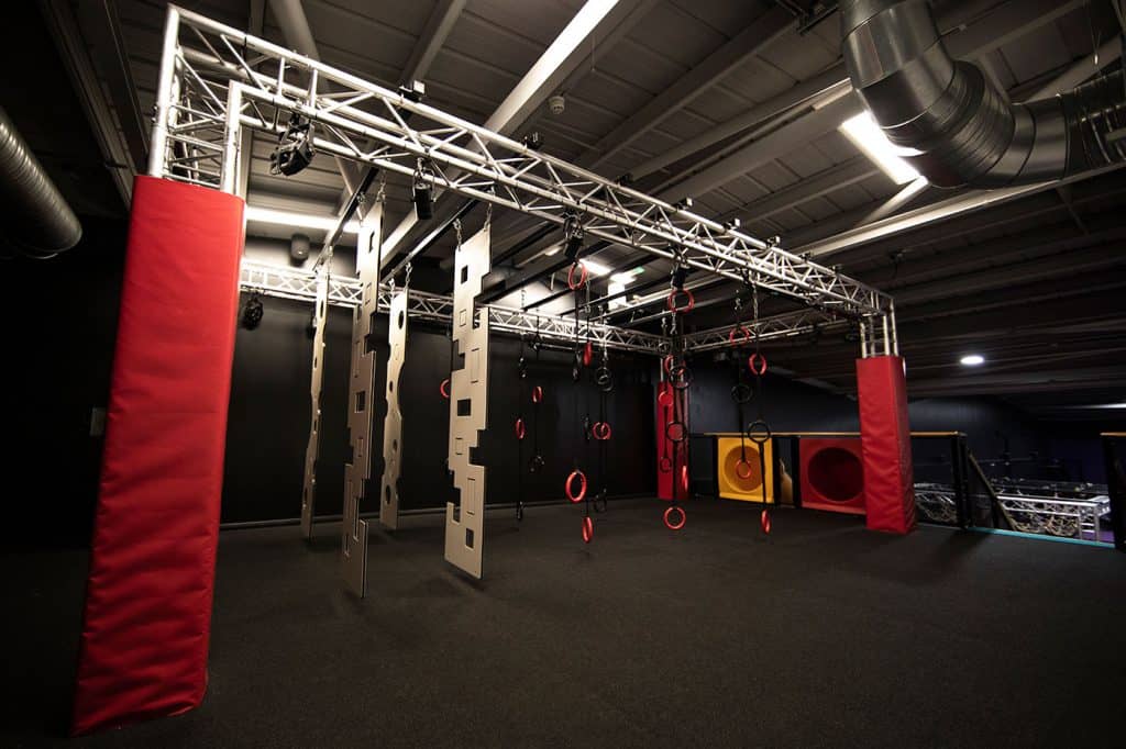 Climbing and obstacle course equipment in an indoor gym with padded flooring for safety.