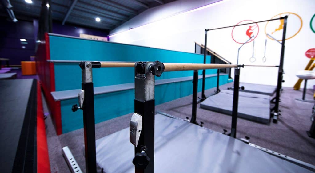 Adjustable balance beam setup in an indoor gymnastics training facility with colorful wall graphics and safety mats.