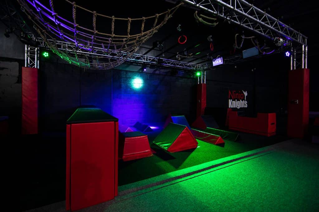 Climbing adventure area with padded obstacles and ropes under colourful LED lighting, designed for kids' ninja training courses.