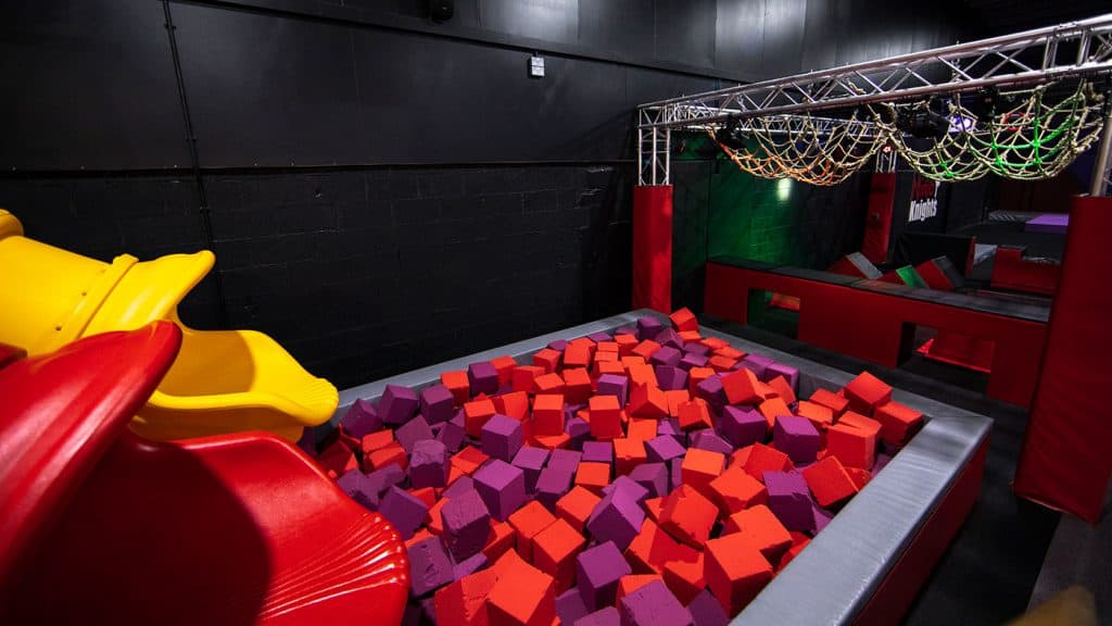Vibrant indoor ninja warrior obstacle course with colourful foam pit, slides, climbing nets, and padded structures for kids' indoor play and adventure activities.