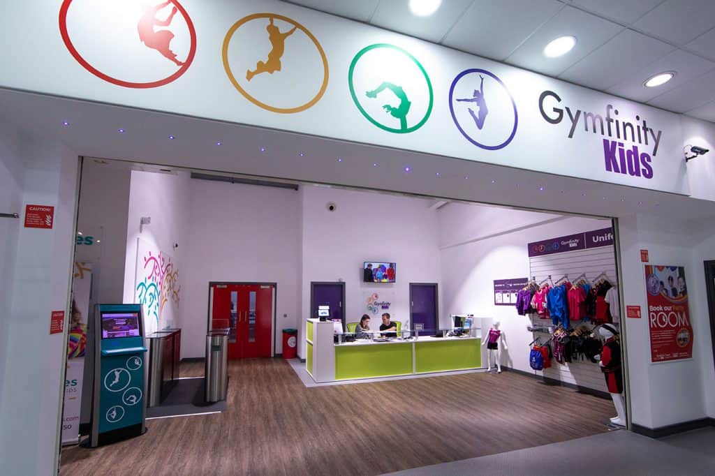 Kids gymnfinity signing area with colourful logo and reception inside a children's gymnastics centre in a shopping mall, UK.
