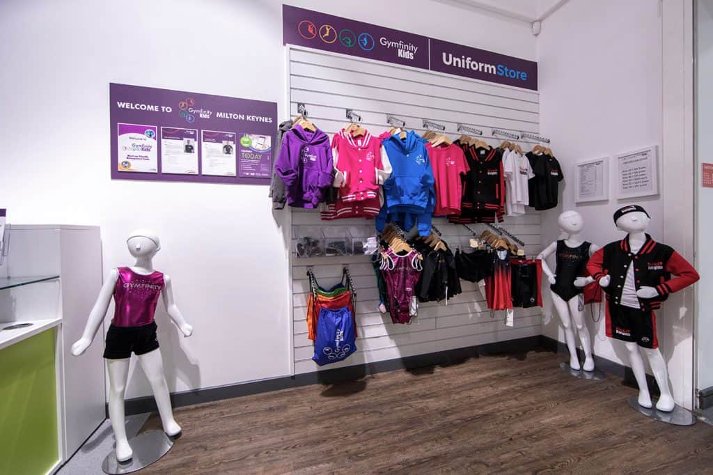 Bright children's sportswear and uniforms displayed on mannequins and wall hooks at Gymfinity Kids' store in Milton Keynes, featuring colourful hoodies, shorts, and accessories for active kids.