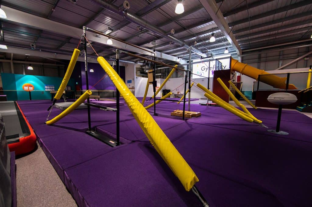 Indoor adventure playground with climbing frames, padded ramps, and slides for kids' fun and physical activity. Brightly coloured and safe for children to explore and play.