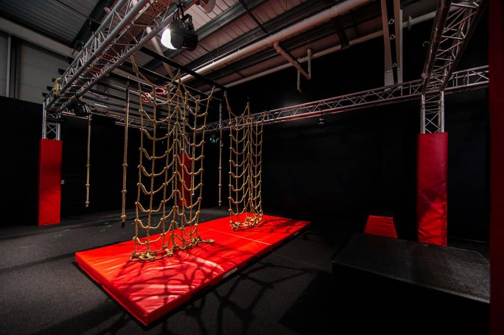 Climbing obstacle course with rope nets and padded landing area at an indoor adventure park. Suitable for children and adults to test agility and strength in a controlled environment.