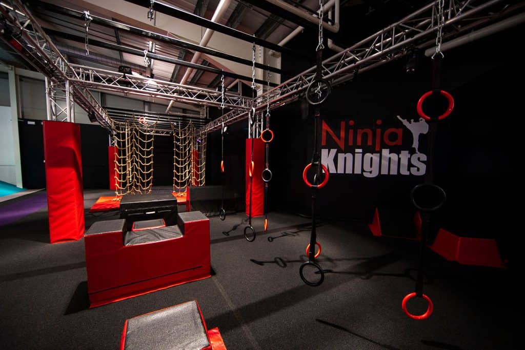 Climbing obstacle course at Ninja Knights indoor activity centre, featuring rings, ropes, and padded platforms for kids' adventure and fitness challenges.