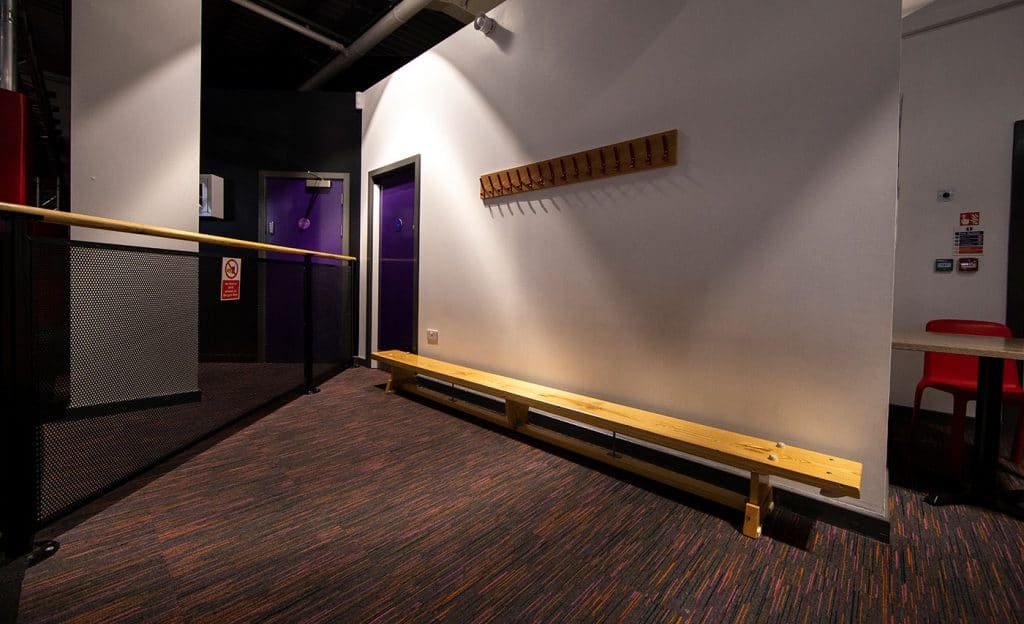 Grooming area with benches and coat hooks, leading to two purple doors, in an indoor sports or recreation centre.
