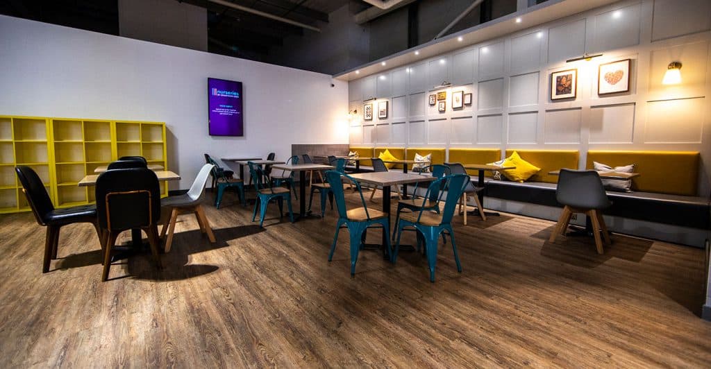 Colourful modern cafe interior with mixed seating arrangements, decorative wall art, warm lighting, and wood flooring, perfect for socialising or casual meetings.