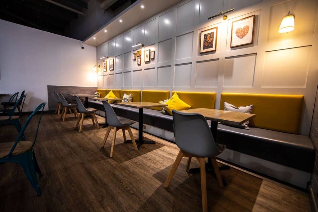 Bright modern café interior with yellow cushioned seating, stylish wall art, and warm lighting creating a cozy and inviting atmosphere.