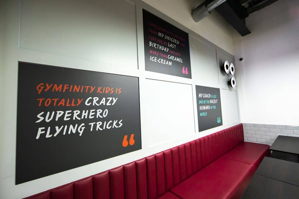 Gymfinity Kids inspirational wall with vibrant motivational quotes and a red cushioned bench in a modern, playful interior.