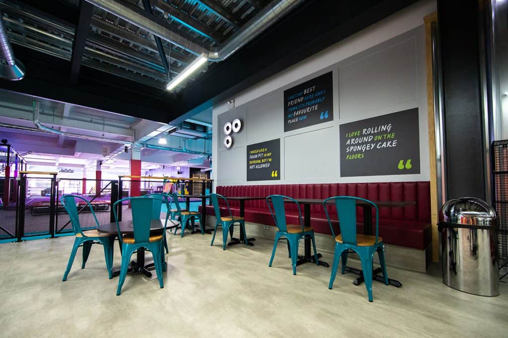 Enjoyable indoor seating area with colourful chairs, wall-mounted inspirational quotes, and a vibrant sports or activity zone in the background at a modern recreational centre.