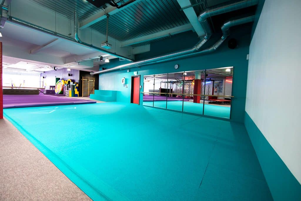 Blue gymnasium flooring and mirrored wall in a fitness studio with vibrant workout equipment and bright lighting, creating an inviting space for dance or exercise classes.
