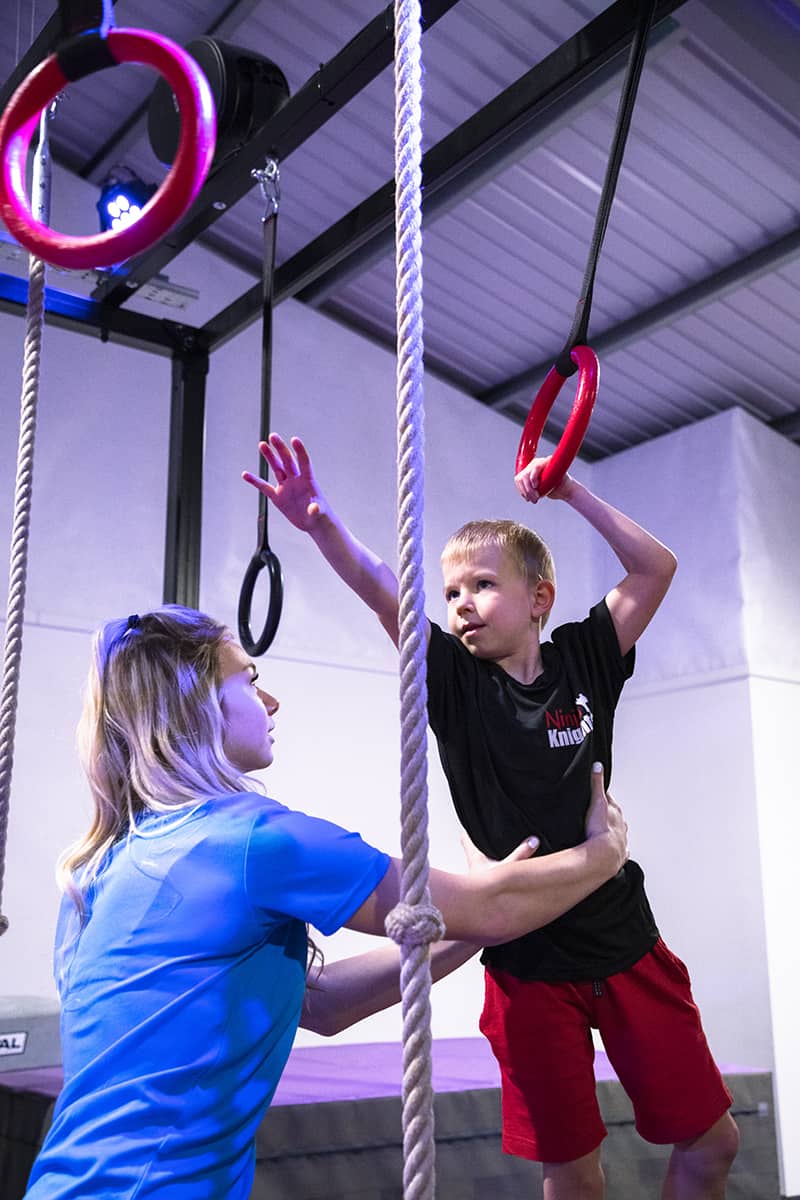 Climber working on grip strength with instructor at indoor gym.