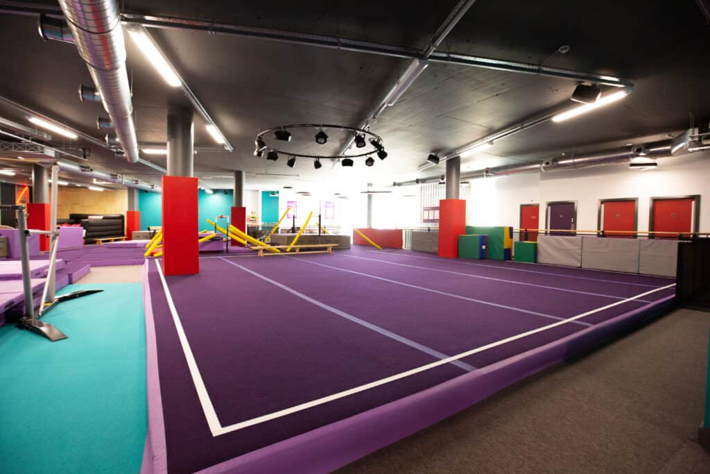 Colorful indoor trampoline park with purple flooring, padded walls, and various obstacle courses in a modern recreational facility for kids and teens.