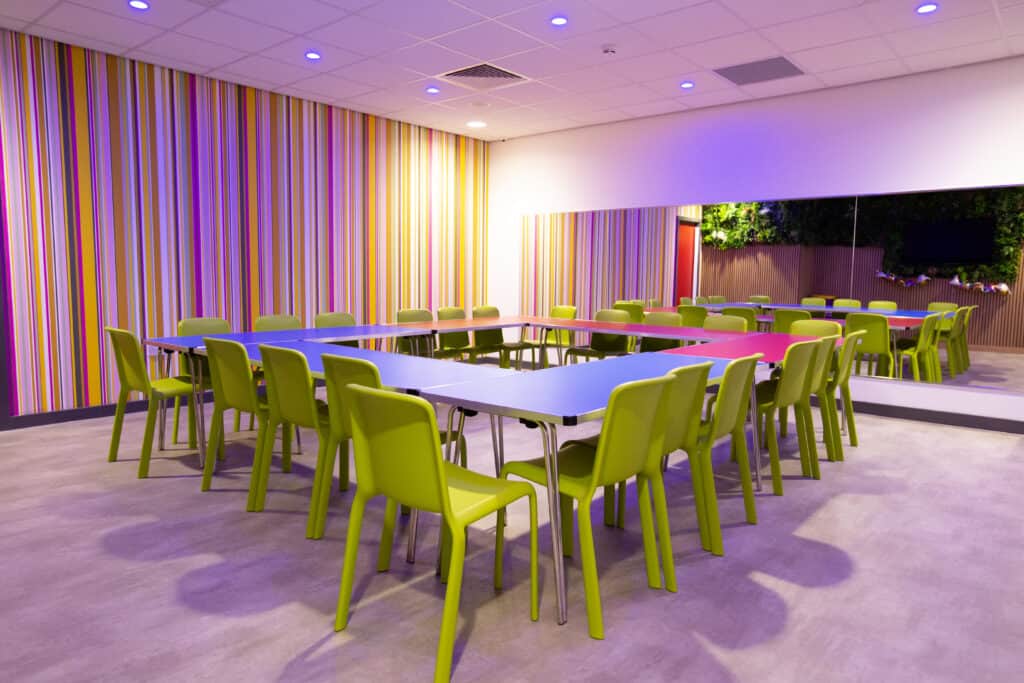 Vibrant conference room with multicoloured striped wall, lime green chairs, and modern lighting ideal for meetings or events.