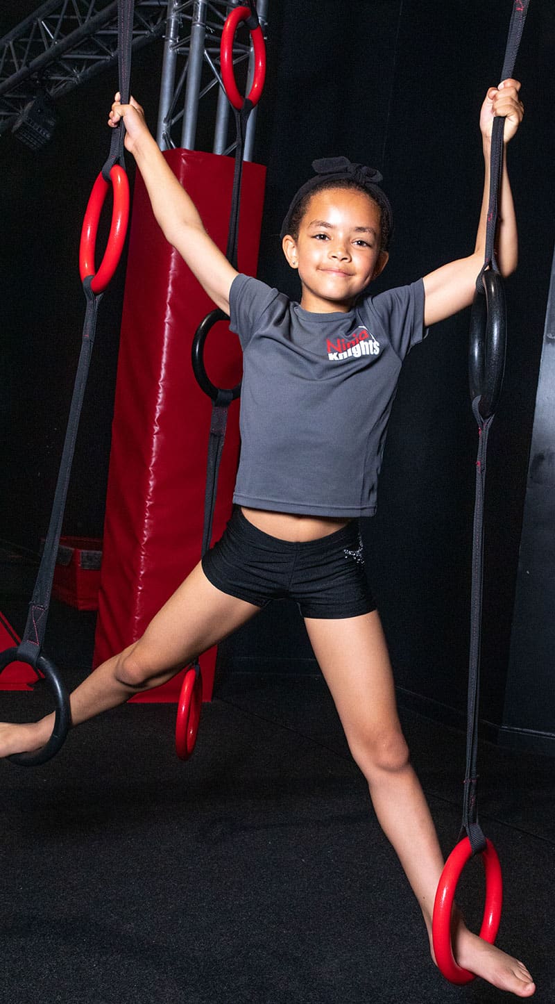 Strength training girl holding gym rings at fitness centre, young girl doing gym workout on gymnastics rings, indoor gym with workout equipment, girl exercising with fitness rings, active girl engaged in physical fitness activities.