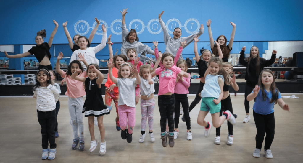 Children and young adults having fun jumping in a dance studio with vibrant energy and smiles.
