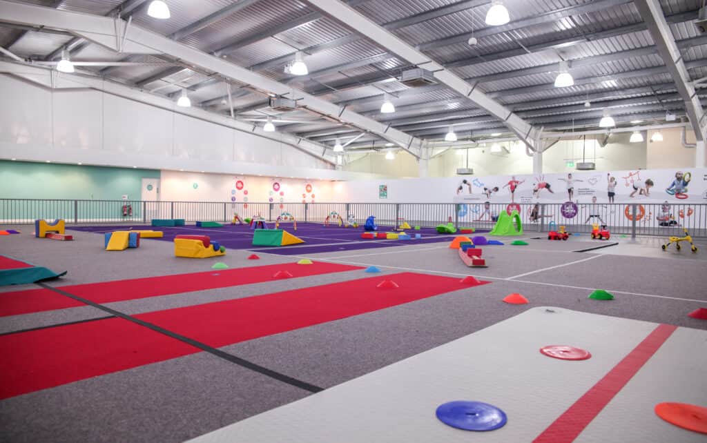 Climbing and sports indoor play area for children with colourful soft mats and training equipment in a spacious gymnasium.