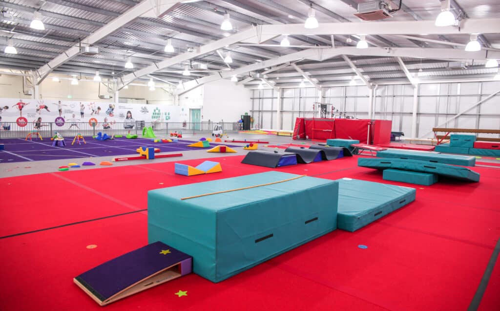 Bright indoor gymnastics and play area featuring colourful padded mats, soft play equipment, and climbing structures designed for children's activities and physical exercise.