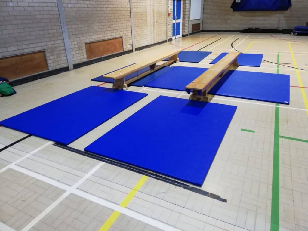 Blue gymnastic mats and wooden benches set up in an indoor sports hall.