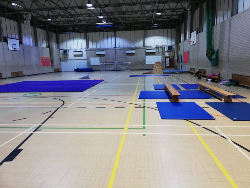 Spacious indoor gymnastics hall equipped with blue mats, benches, and climbing equipment, ready for training or competitions in a well-lit sports facility.