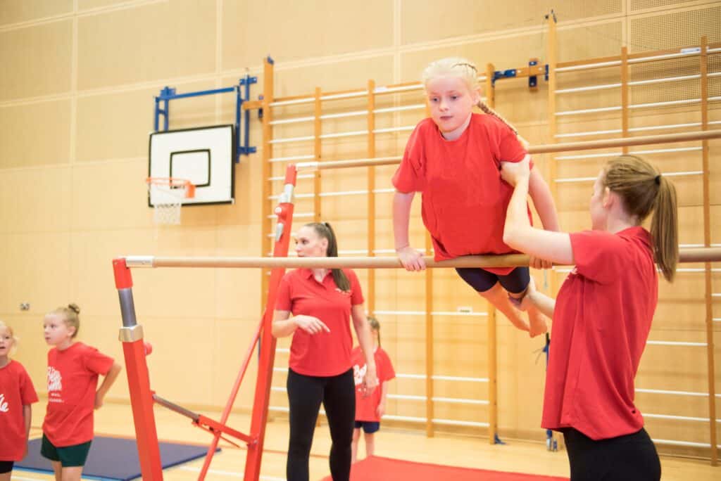 Handstand training on parallel bars in a gymnasium with children and instructor.