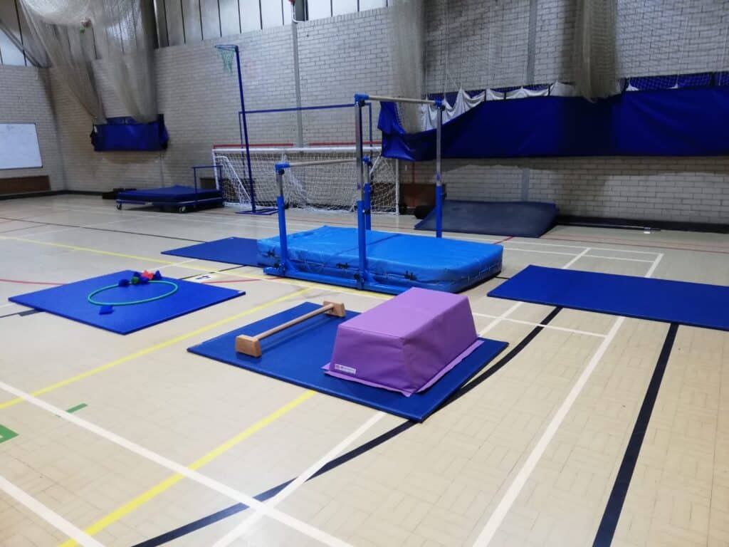 Climbing and gymnastic equipment set up in an indoor sports hall, including mats, a balance beam, and soft landing areas for gymnastics and physical training activities.