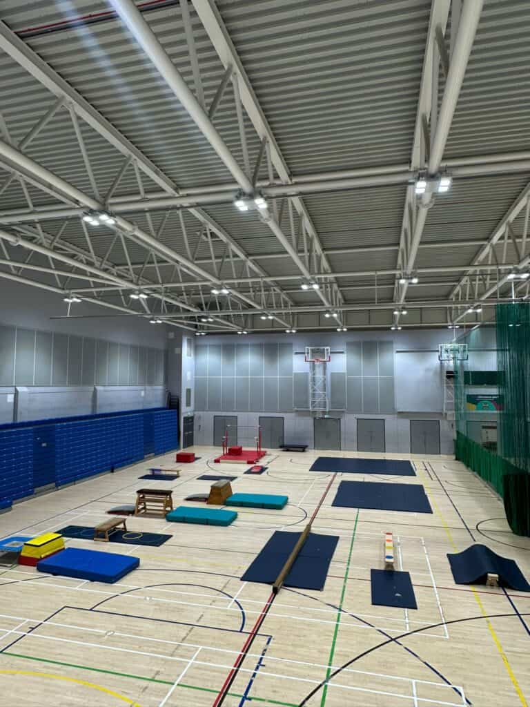 Climbing gym indoor training facility with padded mats, climbing walls, and equipment for fitness and bouldering activities in a spacious hall.