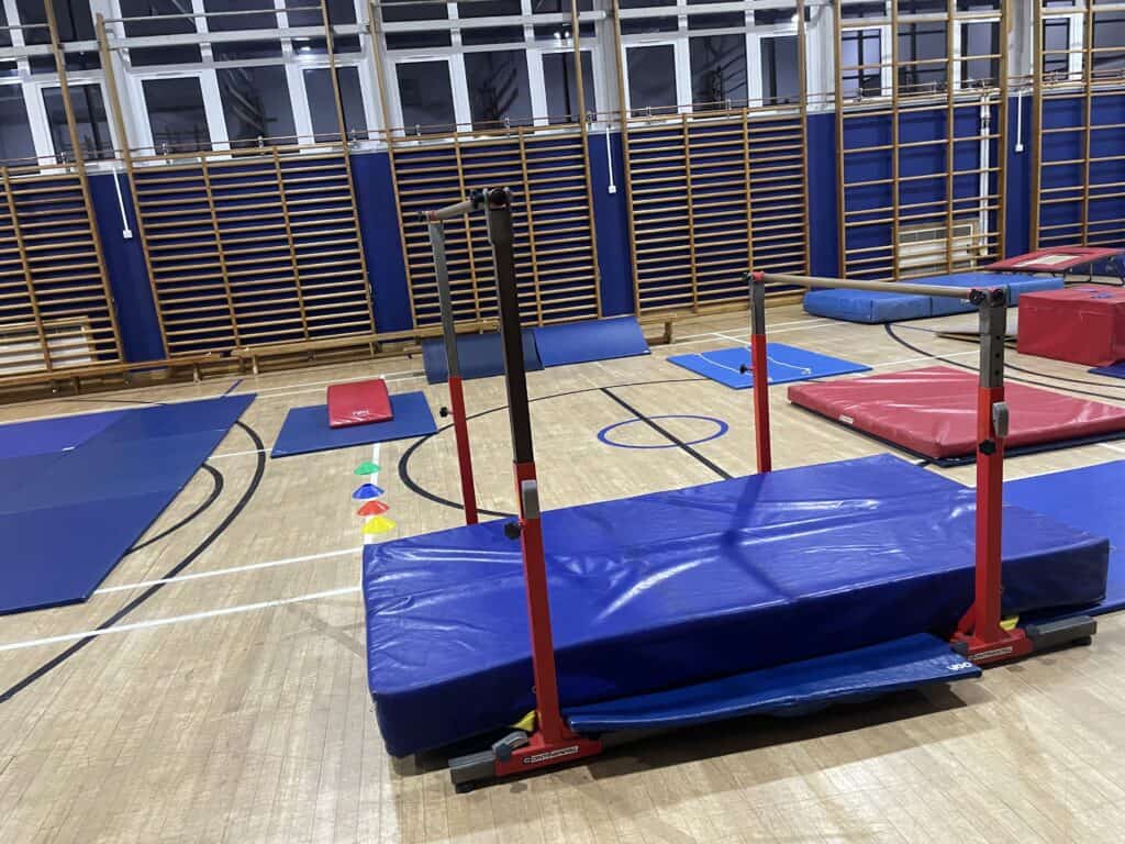 Climbing training area in gym with mats, bars, and agility cones set up for gymnastics or parkour practice.
