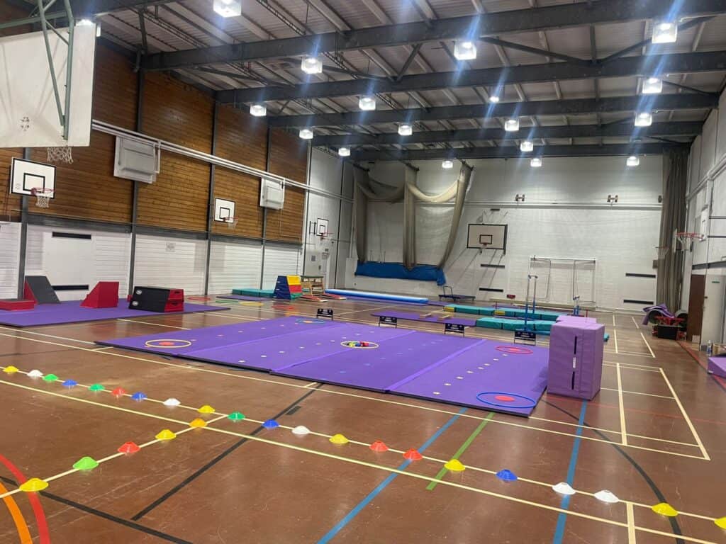 Gymnastics training equipment, foam pits, mats, and basketball hoops in an indoor sports hall for gymnastics practice and competitions.