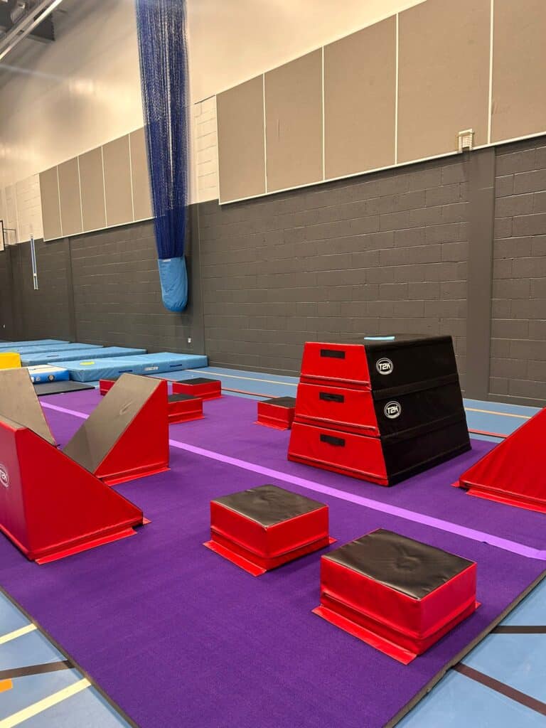 Red and black padded gymnastic training equipment on a purple mat in a sports hall.