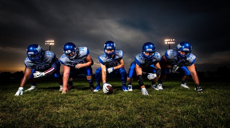 Team of American football players in blue uniforms preparing for game on a grassy field under evening sky.