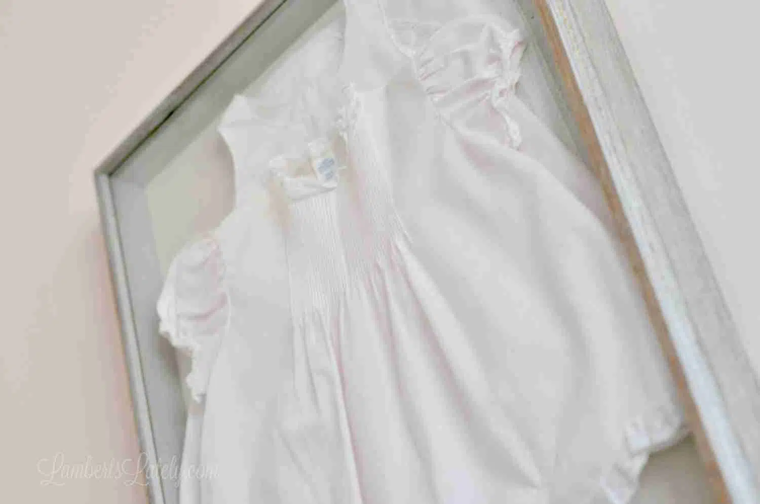 looking up on a pink baby dress hanging on a pink wall in a shadow box.
