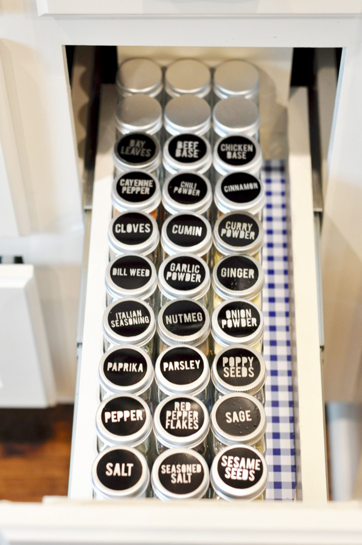 open spice cabinet with black glass spice jars lined in rows.
