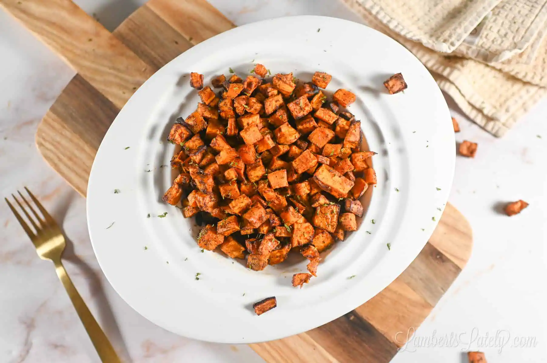 air fryer sweet potato cubes in a bowl on a cutting board, with a fork and a cloth napkin.
