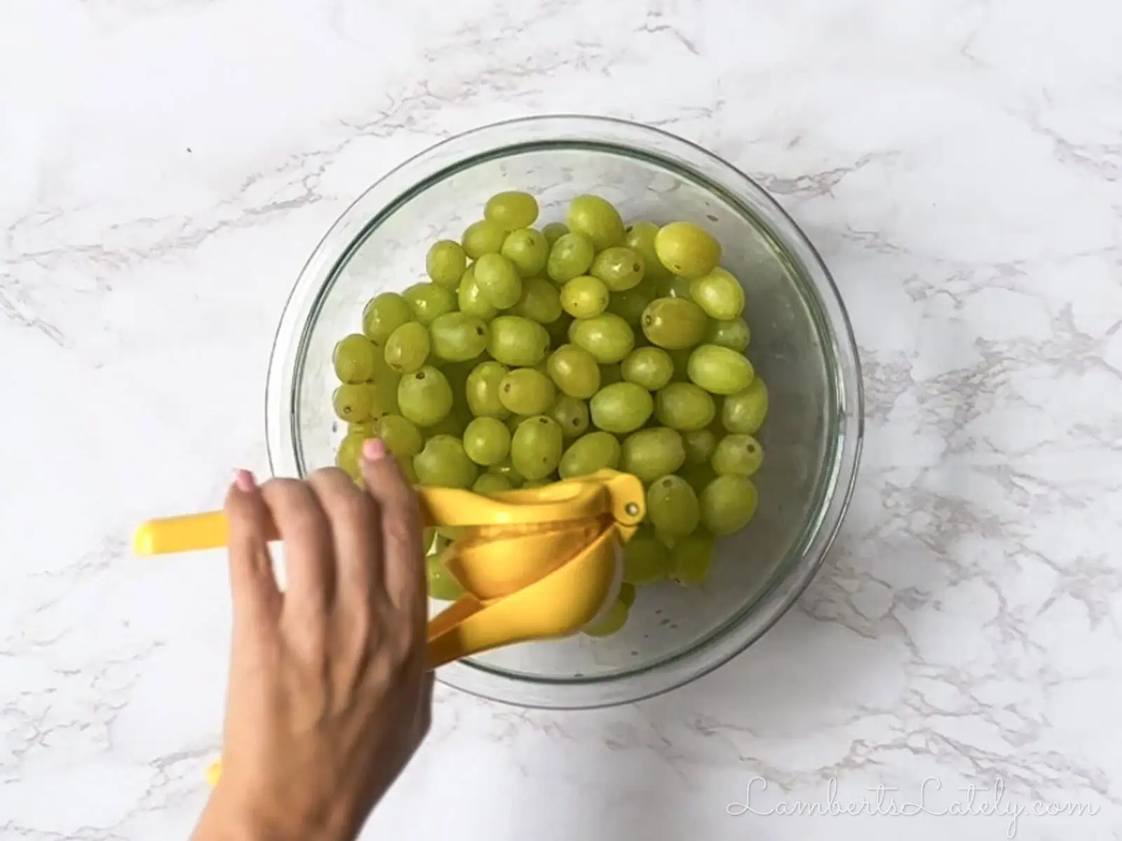 squeezing lemon juice over green grapes in a bowl.