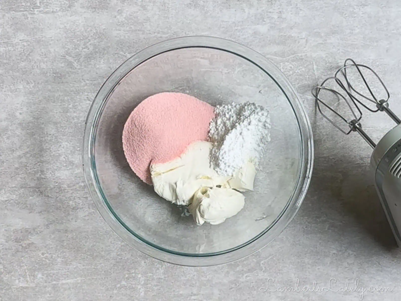 jello mix, cream cheese, and powdered sugar in a bowl, next to a hand mixer.
