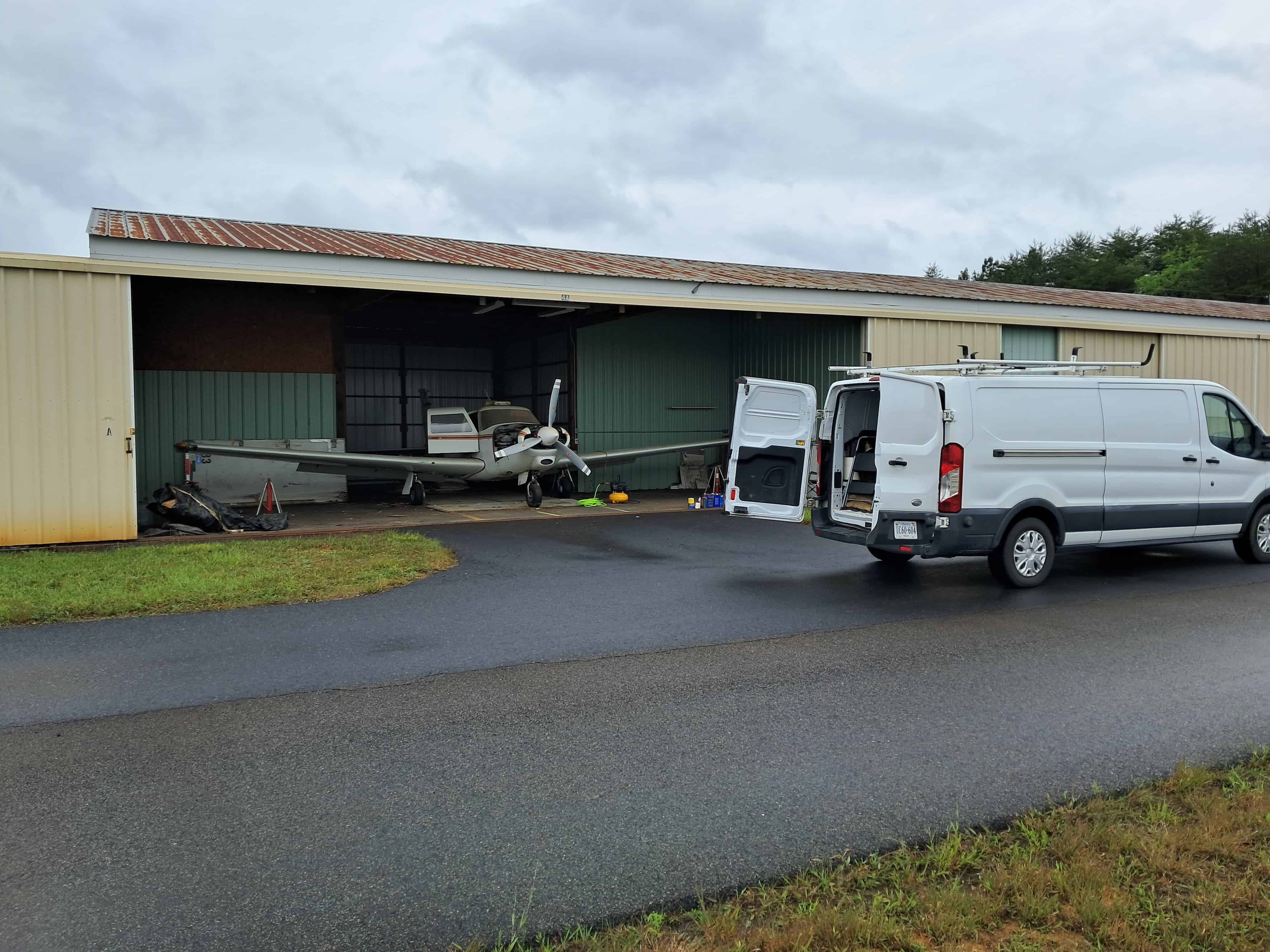 Aircraft maintenance hangar with van and small plane outside on a cloudy day.