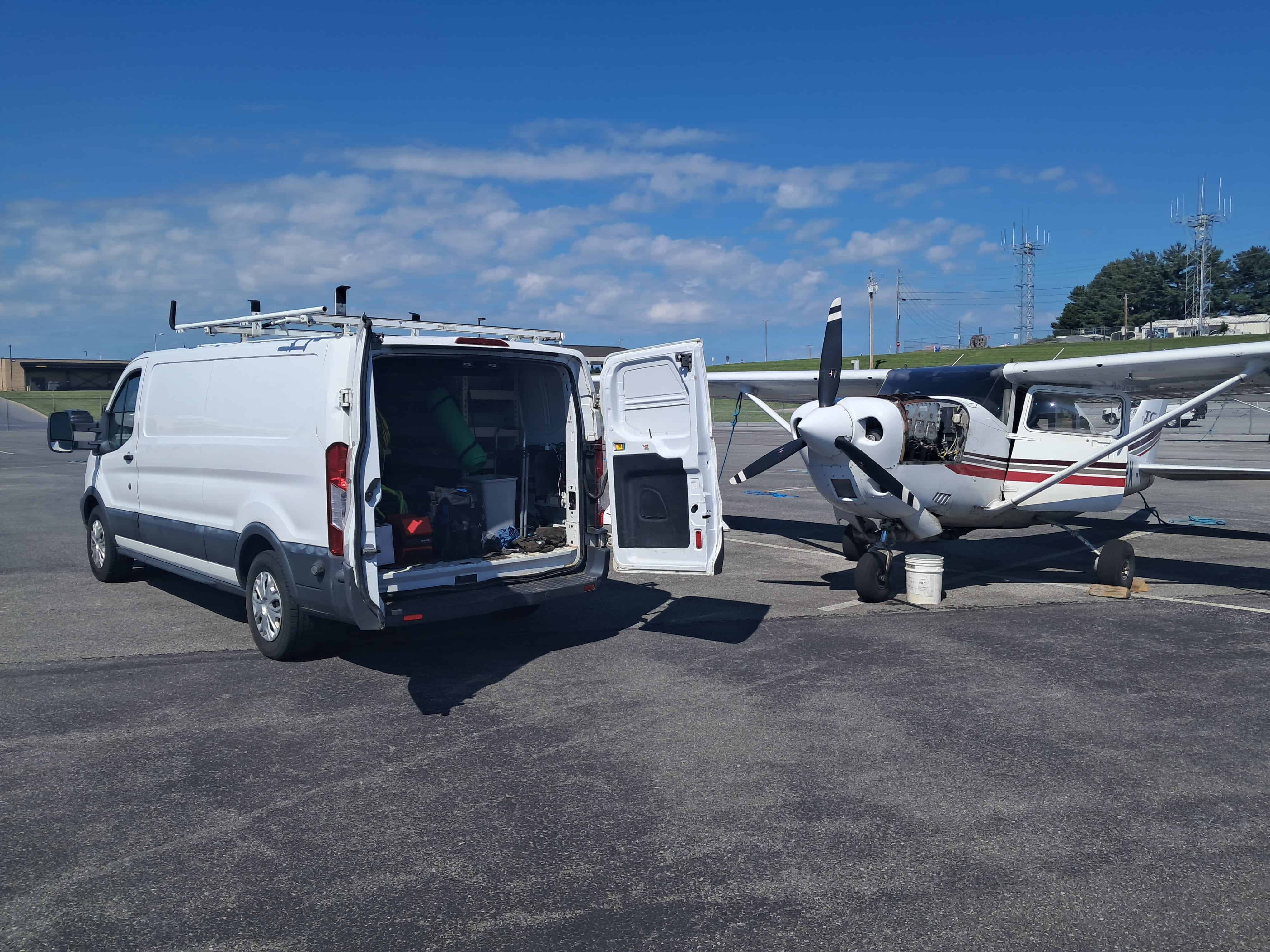 Aircraft maintenance van with open door parked next to a small propeller plane.