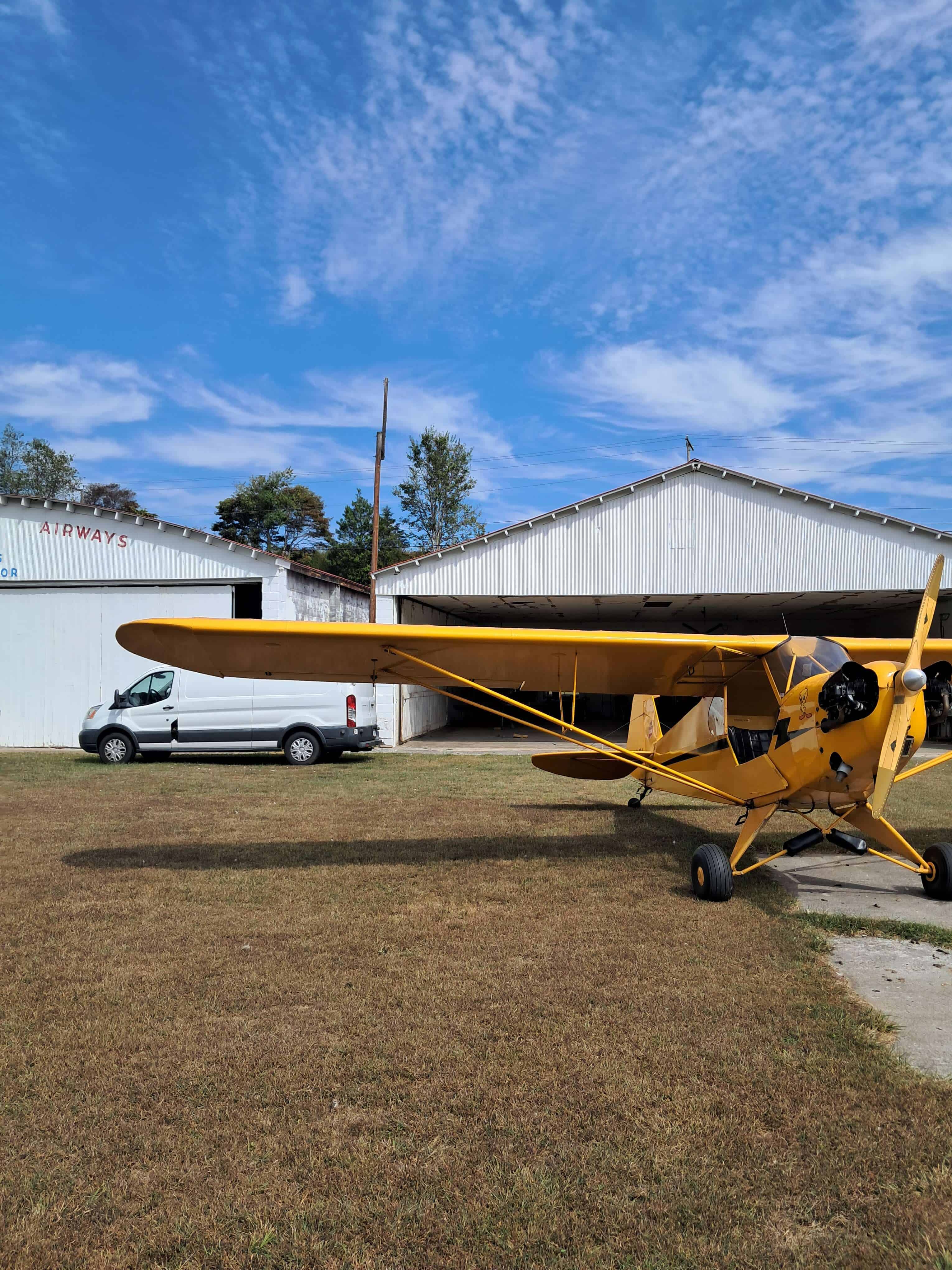 Yellow light aircraft parked on the grass near hangar at New Flight Aviation.